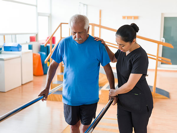 A female nurse helping a senior man to walk in the parallel bars.