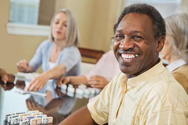 Happy senior man playing dominoes with friends at home